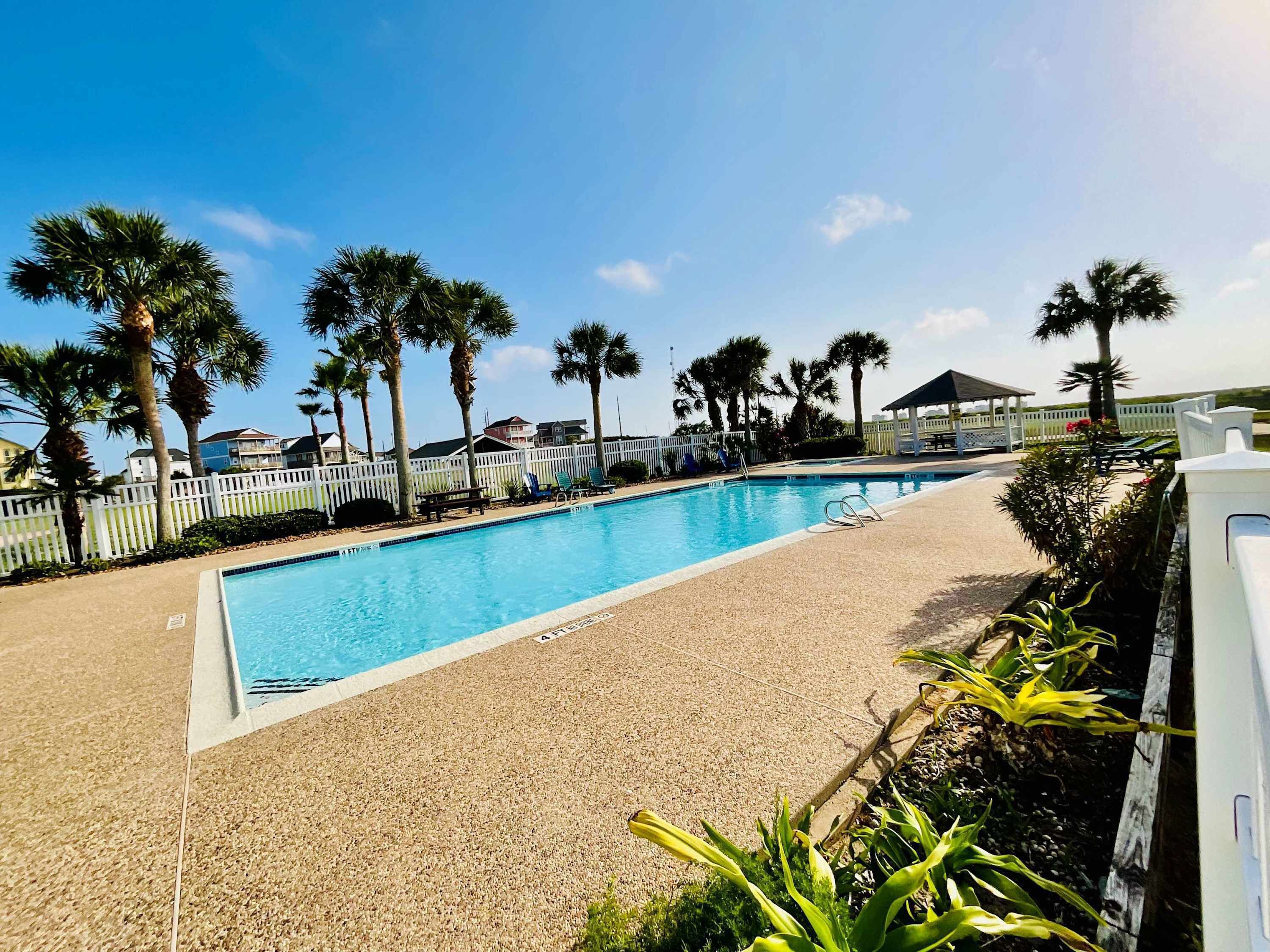 Una piscina con una valla blanca, palmeras y un cielo azul despejado.