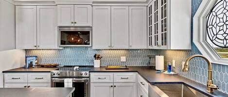 A modern kitchen with white cabinets, stainless steel appliances, and a blue-tiled backsplash.