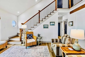 A spacious living area with a staircase, a wicker chair, a striped sofa, and a lamp. - Spoonbill at West Bay (Galveston)
