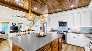 A modern kitchen with a large island, white cabinetry, and a wooden ceiling. - Spoonbill at West Bay (Galveston)