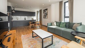Ein modernes Wohnzimmer mit einer Küche, Essbereich und einem grünen Sofa mit gemusterten Kissen.
