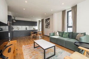 Ein modernes Wohnzimmer mit einer Küche, Essbereich und einem grünen Sofa mit gemusterten Kissen.