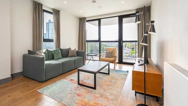 Ein modernes Wohnzimmer mit einem grauen Sofa, einem Couchtisch, einer Holzkommode und einem großen Fenster mit Blick auf die Stadt.