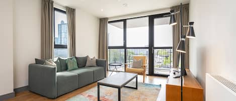 A modern living room with a grey sofa, a coffee table, a wooden cabinet, and a large window with a view of the city.