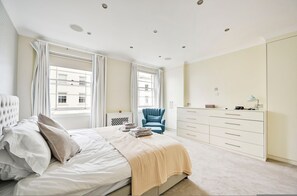 Une chambre à coucher avec un lit, une chaise, une commode et une fenêtre avec des rideaux.