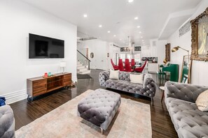 A modern living room with a flat-screen TV, a wooden console, and a grey tufted sofa set.