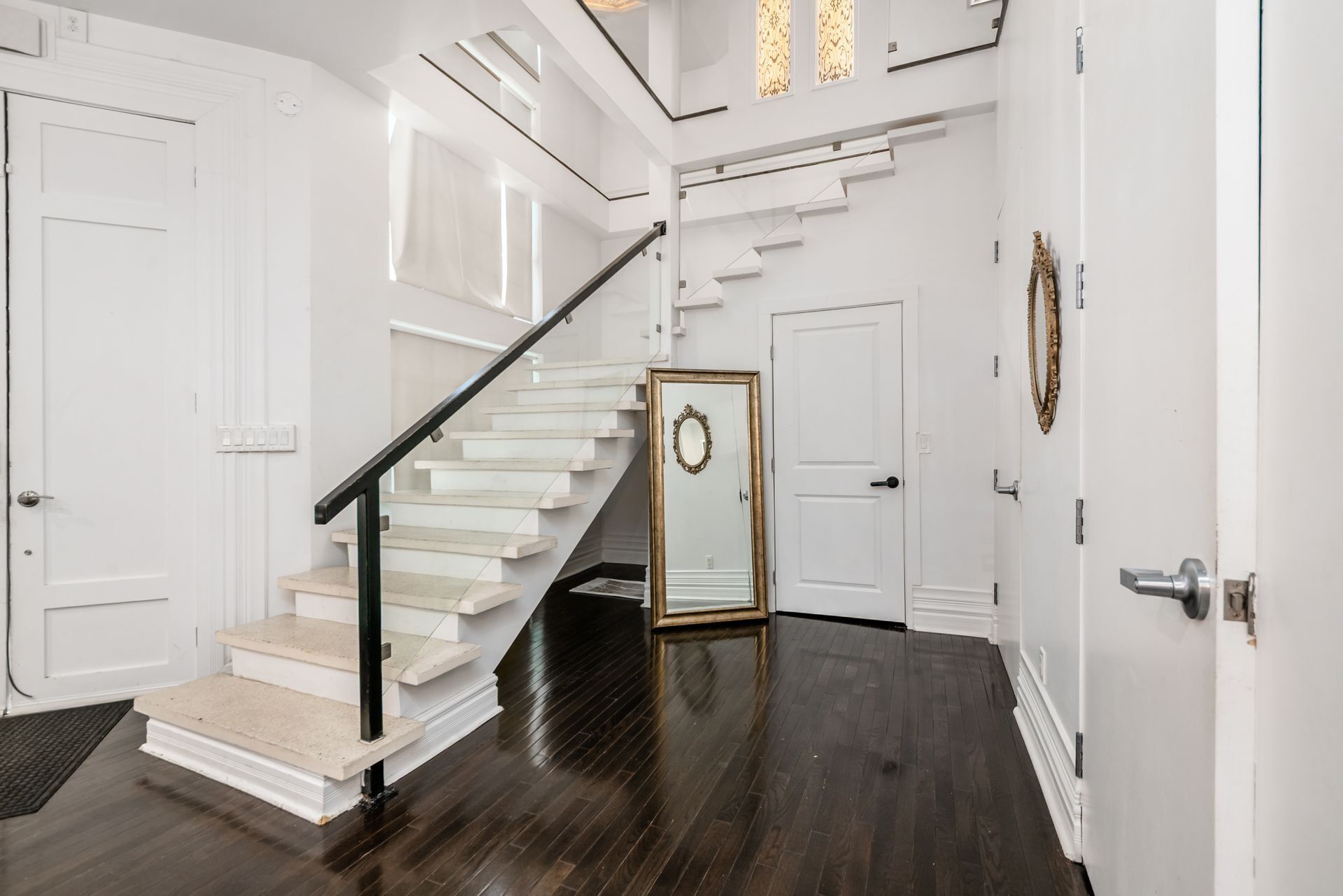 A staircase with a black handrail, white walls, and a dark wooden floor.