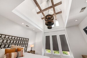 A bedroom with a bed, a nightstand, a lamp, a wooden ceiling, and a window with blinds.