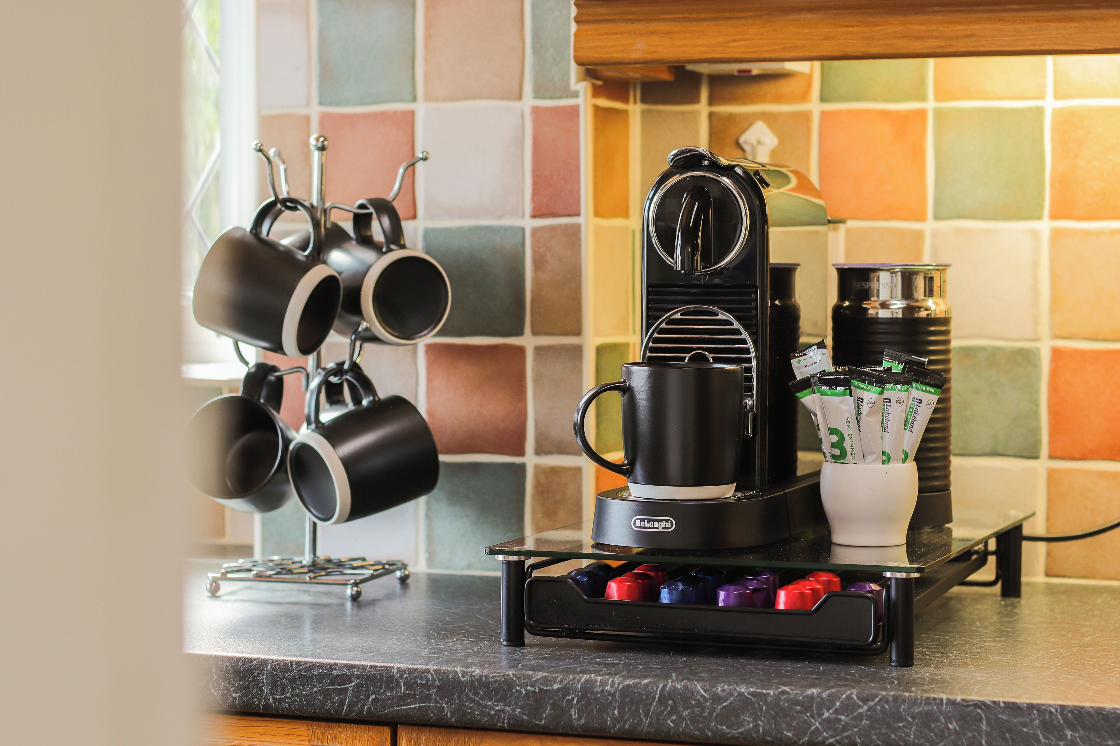 Une machine à café posée sur un plan de travail de cuisine, avec un porte-tasses et un support pour les capsules de café.
