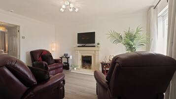 A living room with leather recliners, a flat-screen TV, a fireplace, and a large plant.