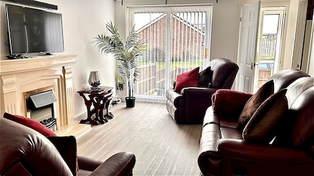 A living room with a fireplace, leather sofas, a television, and a large potted plant.. Peaceful 2-Bed Bungalow with Garden and Parking