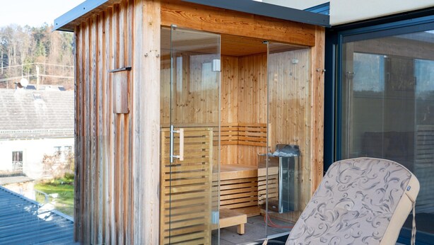A wooden sauna with glass doors, a bench, and a chair. - Apartment Near Graz With Sauna (Premstätten bei Vasoldsberg)