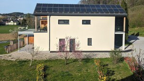 A modern house with a solar panel roof, a small garden with flowers, and a view of a rural area. - Apartment Near Graz With Sauna (Premstätten bei Vasoldsberg)