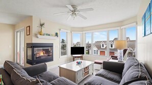 Ein Wohnzimmer mit Kamin, Deckenventilator, Fernseher und großem Fenster.