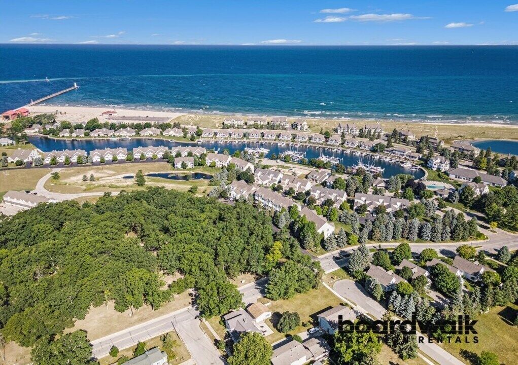 An aerial view of a coastal residential area with houses, a marina, and a beach.