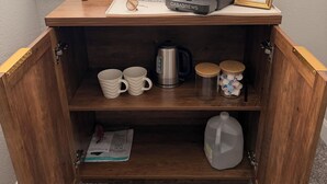En kaffestation med kaffemaskine, kopper, elkedel og et velkomstskilt i ramme.