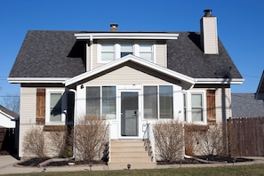 A two-story house with a front porch, a chimney, and a small front yard with shrubs. - Kenosha Retreat - Created to Help You Relax (Kenosha)