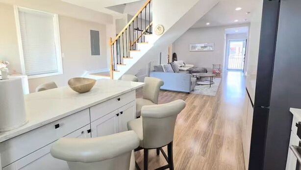 A modern kitchen with a wooden staircase, a dining area with a sofa, and a view of the living room. - Dockside Den,  Waterside 3BR, Close to All (Atlantic City)