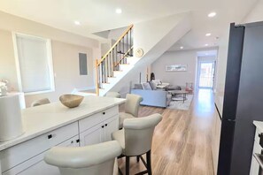 Eine moderne Küche mit einer Holztreppe, einem Essbereich mit einer Couch und Blick zum Wohnzimmer.