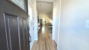 A hallway with a dark wooden door, white walls, and a wooden floor leading to a kitchen area. - Dockside Den,  Waterside 3BR, Close to All (Atlantic City)