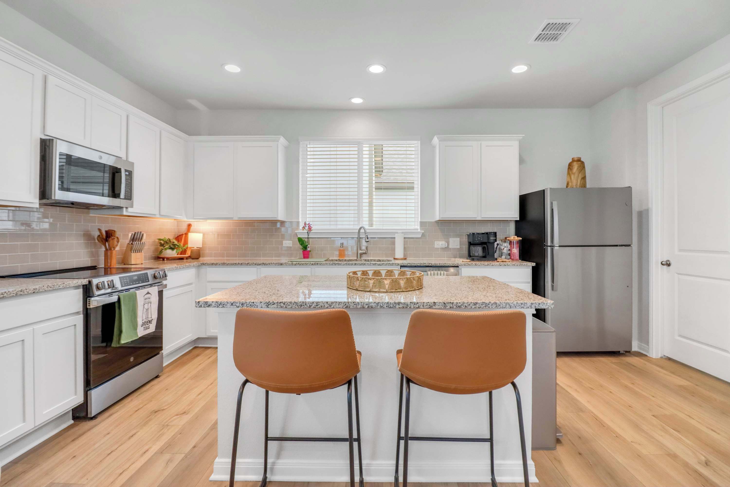 A modern kitchen with white cabinets, stainless steel appliances, and a central island with two bar stools.