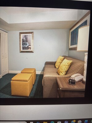 Ein Zimmer mit einem Bett, einem Nachttisch mit Lampe, einem gerahmten Bild an der Wand und einem Fenster.