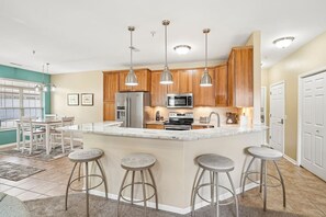 A modern kitchen with wooden cabinets, stainless steel appliances, and a central island with bar stools. - Whispering Waters at Delton Grand - Ground Floor (Wisconsin Dells)