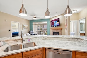 A modern kitchen with a marble countertop, stainless steel sink, wooden cabinets, and a built-in dishwasher. - Whispering Waters at Delton Grand - Ground Floor (Wisconsin Dells)