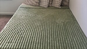 Sängyssä on uurtekuvioitu vihreä pä ällinen, ikkunasta avautuu näkymä vehreään maisemaan ja seinä on maalattu vaalealla värillä.