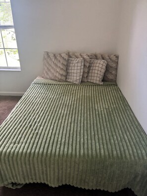 A bed with a ribbed green cover, a window with a view of greenery, and a wall with a light color. - Marvelous 1-bedroom estate with AC in Palm Coast (Palm Coast)