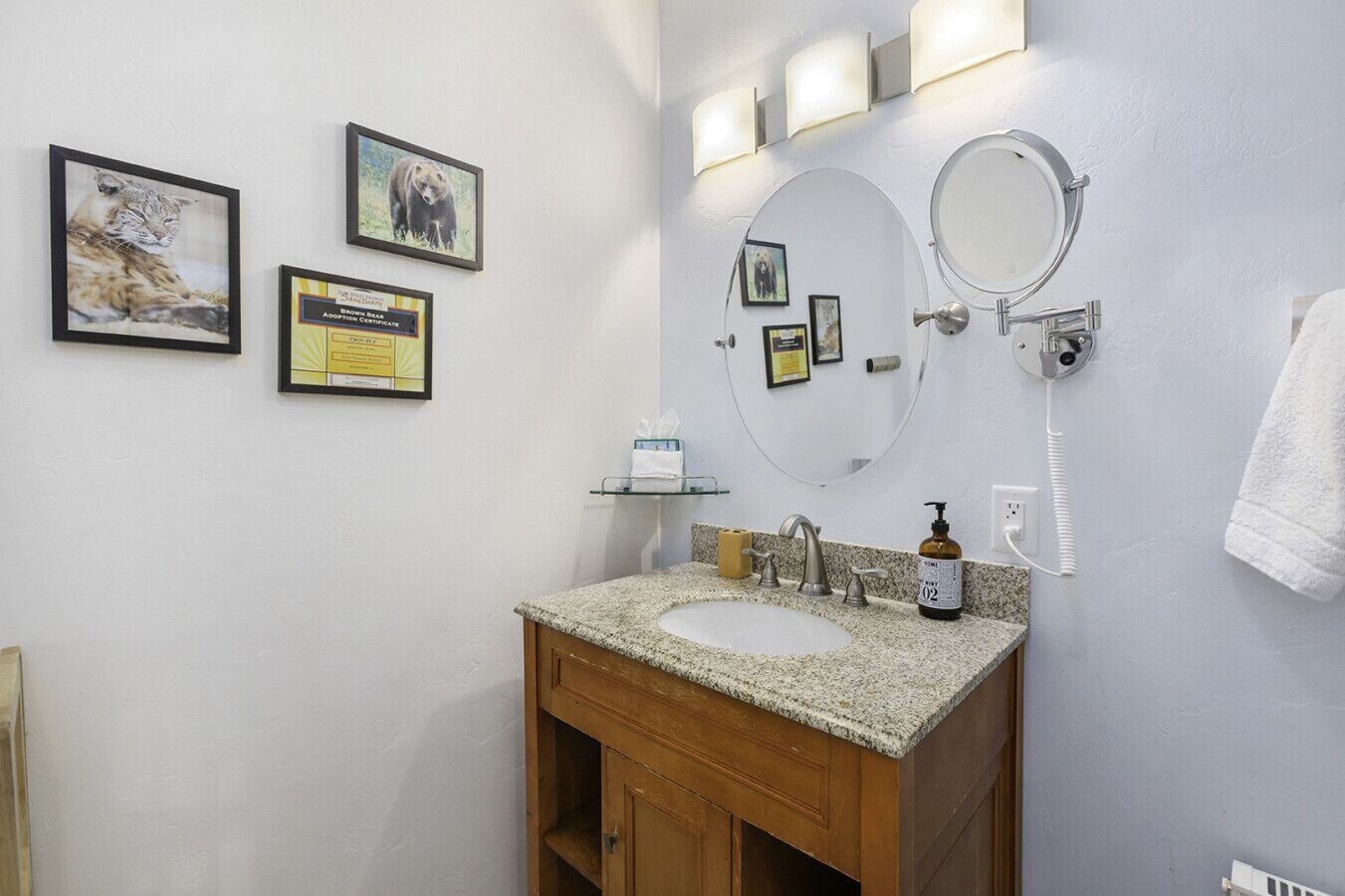 Une salle de bain avec un lavabo en granit, un meuble en bois, un miroir et des tableaux encadrés accrochés au mur.