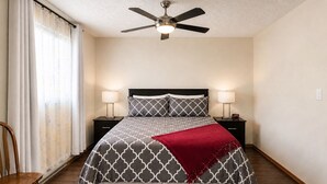 Un dormitorio con una cama, dos mesitas de noche, un ventilador de techo y una silla.