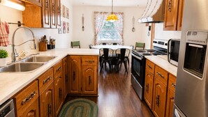 Una cocina con gabinetes de madera, electrodomésticos de acero inoxidable, un comedor con mesa y sillas, y un tapete estampado.