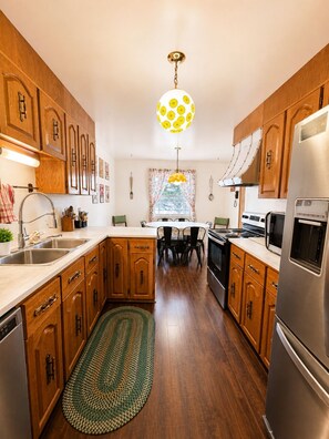 A kitchen with wooden cabinets, stainless steel appliances, a dining area with a table and chairs, and a patterned rug.