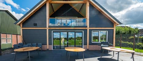 A two-story building with a flat roof, large windows, and an outdoor patio area with tables and chairs.