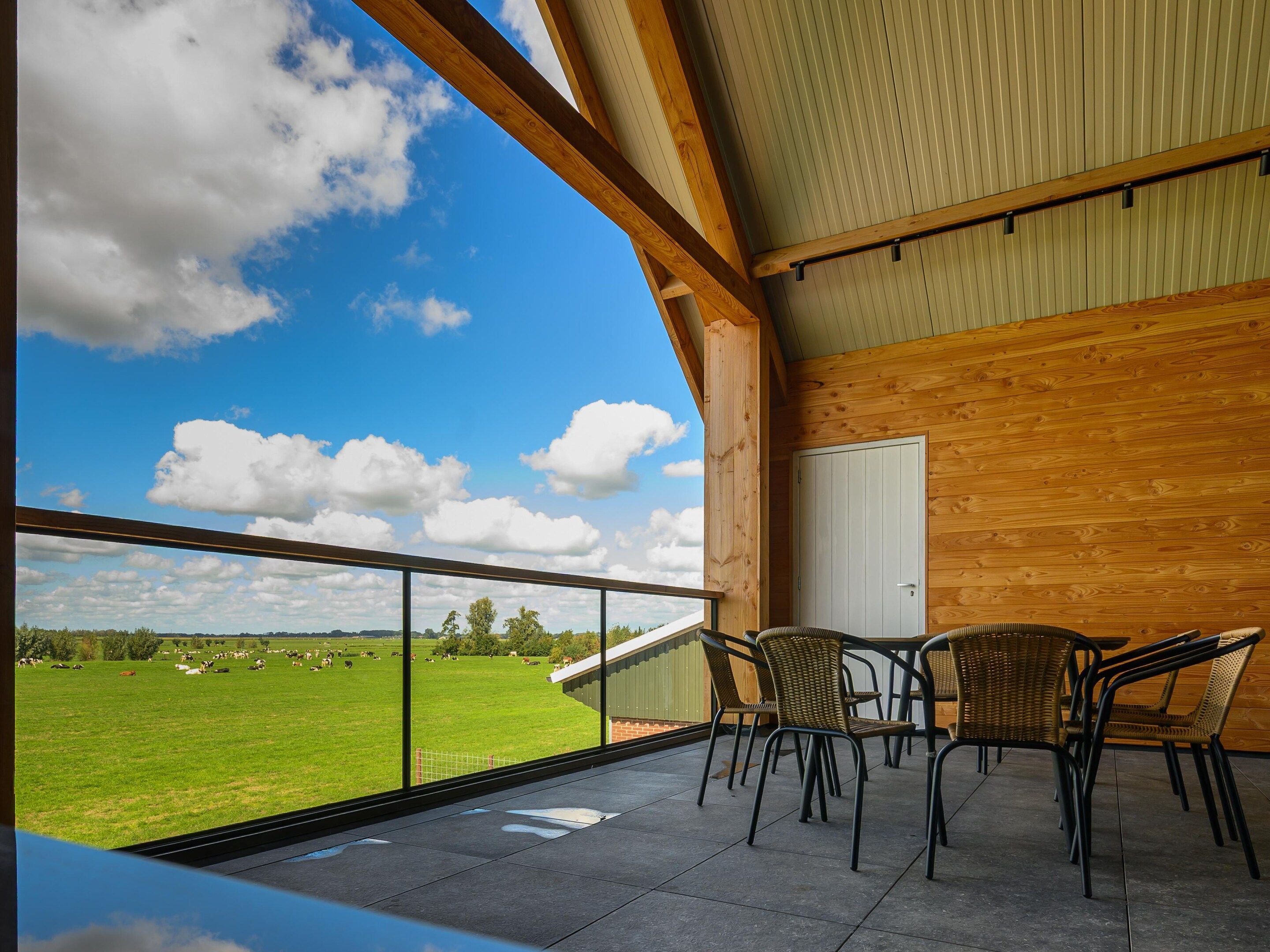 A balcony with a view of a green field and cows, wooden walls, and a table with chairs.