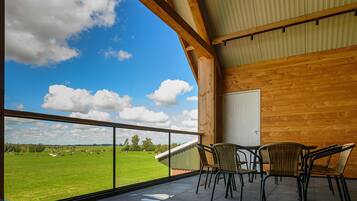 A balcony with a view of a green field and cows, wooden walls, and a table with chairs.