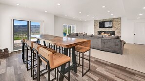 A modern kitchen with a large island, bar stools, a built-in fireplace, and a stone accent wall. - 7BR Mountain View Home | Private Hot Tub | Lake & Resort Proximity | Sleeps 16 (Eden)