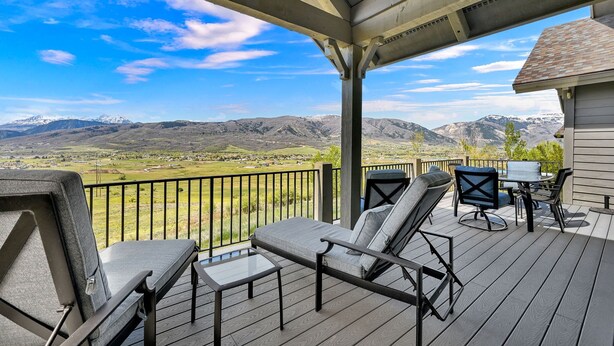 A covered outdoor area with a view of mountains, a patio with a table and chairs, and a lounge chair. - 7BR Mountain View Home | Private Hot Tub | Lake & Resort Proximity | Sleeps 16 (Eden)