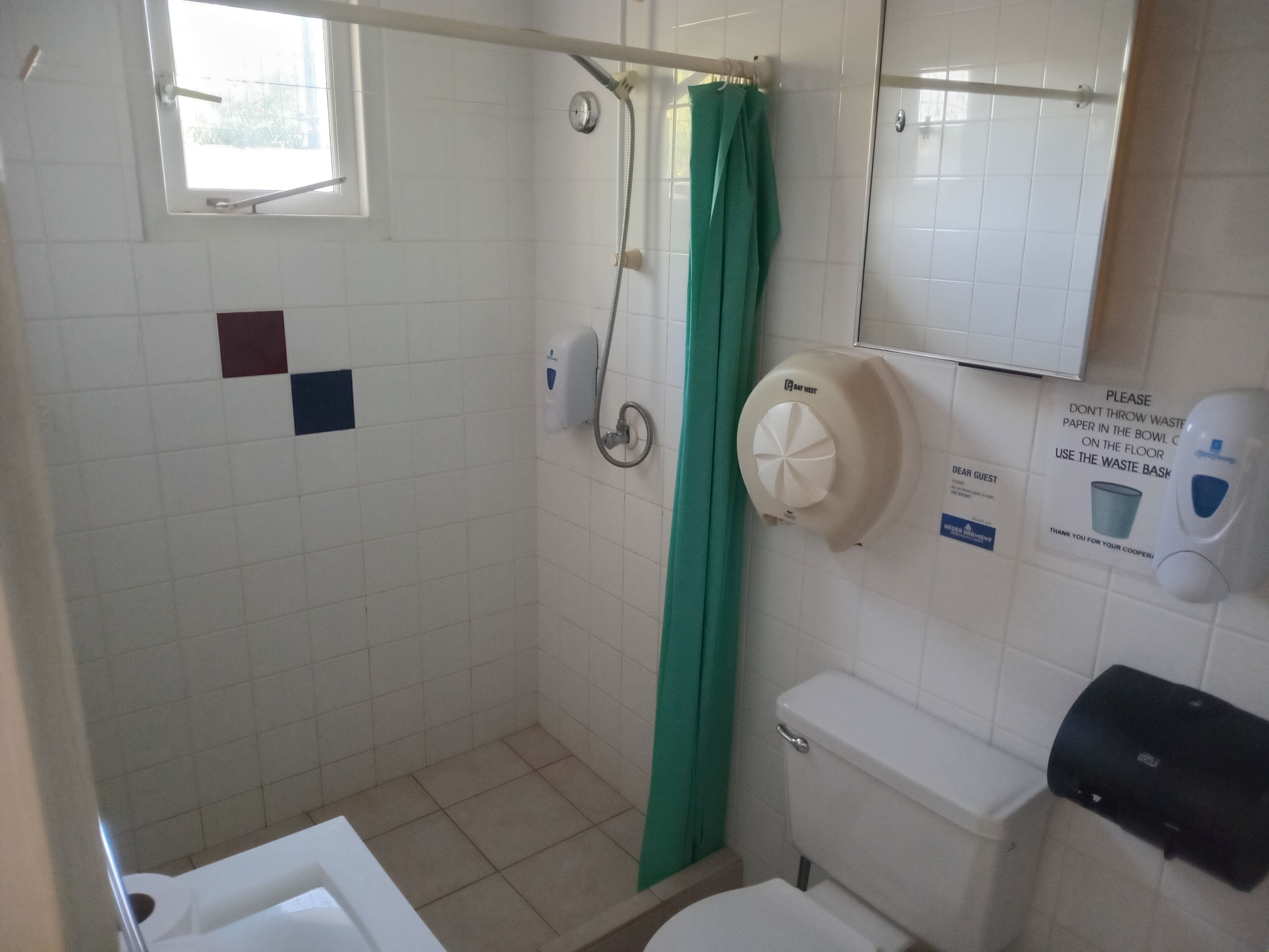Un baño con ducha, inodoro y dispensador de gel hidroalcohólico.