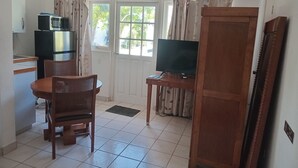 A compact living space with a kitchenette, a dining area with a table and chairs, a television on a stand, and a sliding door leading to an outdoor area.