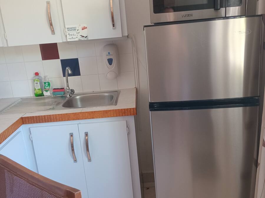 Een keuken met witte kasten, een roestvrijstalen koelkast, een magnetron, een spoelbak en een stoel.
