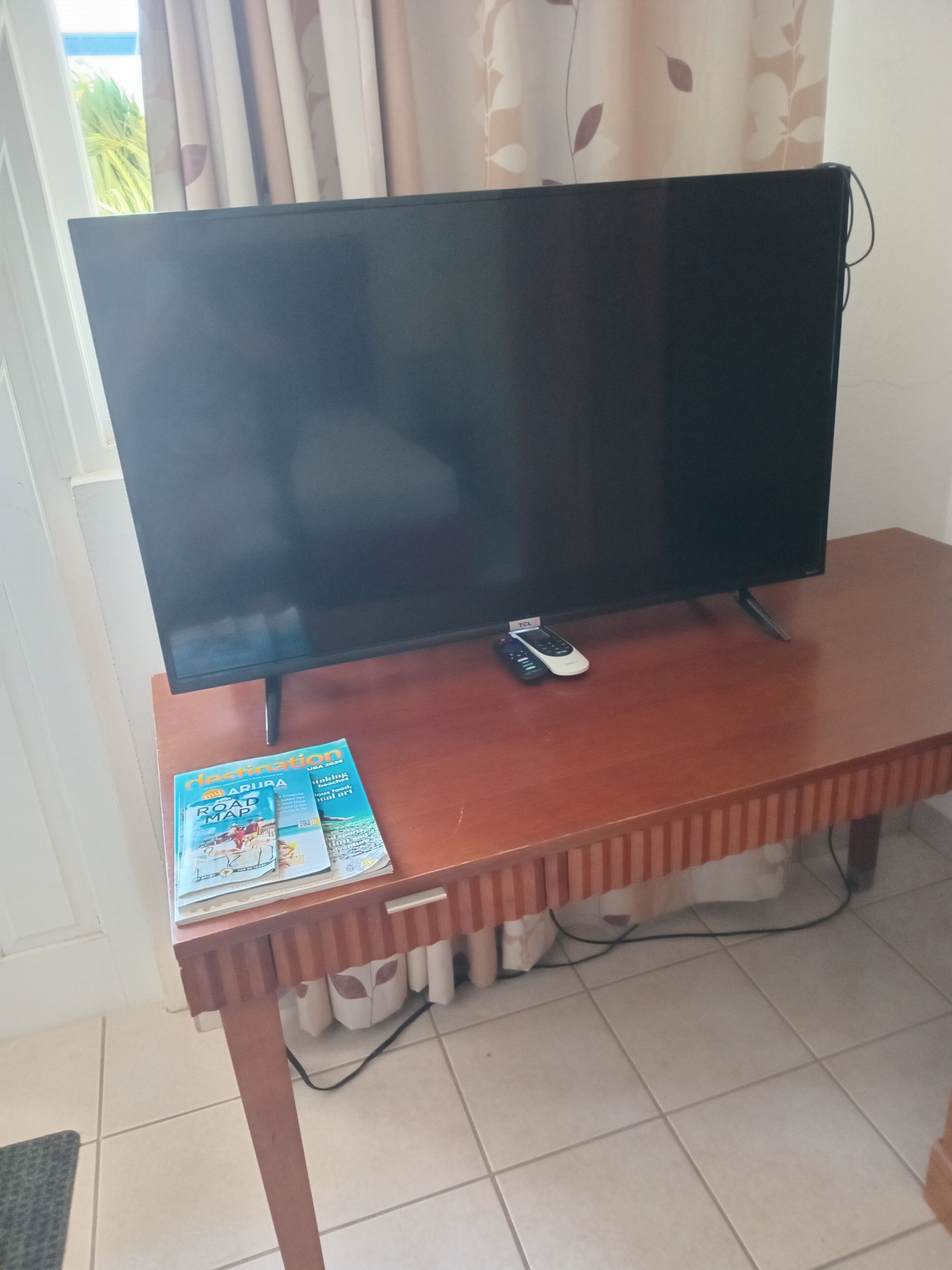 Un televisor sobre un soporte de madera, un control remoto y una guía de viajes sobre el soporte.