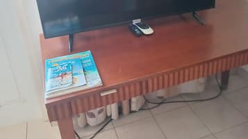 Un televisor sobre un soporte de madera, un control remoto y una guía de viajes sobre el soporte.