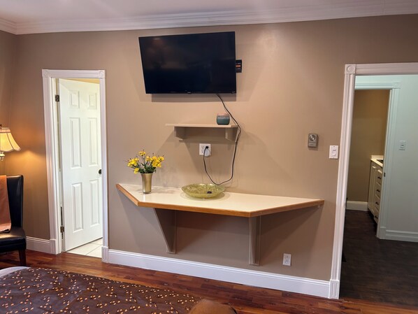 Een kamer met een tv aan de muur, een klein plankje, een vaas met bloemen en een deur.