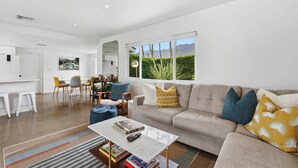 A modern living room with a sofa, coffee table, and a dining area with chairs and a table. - Mountain View Retreat - Pool, Palms, and Peace (Palm Springs)
