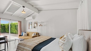 A bedroom with a bed, a sofa, a table, and a view of greenery outside. - Mountain View Retreat - Pool, Palms, and Peace (Palm Springs)