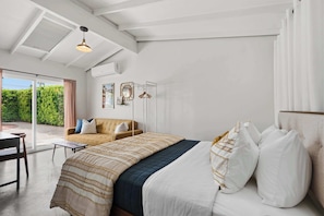 A bedroom with a bed, a sofa, a table, and a view of greenery outside. - Mountain View Retreat - Pool, Palms, and Peace (Palm Springs)