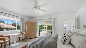 A bedroom with a bed, a ceiling fan, a window with curtains, a table with chairs, and a view of the outside. - Mountain View Retreat - Pool, Palms, and Peace (Palm Springs)