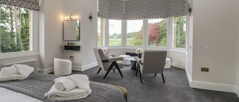 Une chambre d’hôtel avec un grand lit, deux chaises, une petite table, un miroir et une vue sur l’extérieur.